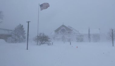 Snow-covered Corpus Christi Church in Sandwich, Massachusetts, in the early morning of Feb. 23, 2026, as an American flag flies in the blizzard conditions.