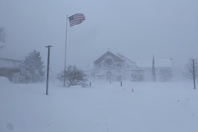 Snow-covered Corpus Christi Church in Sandwich, Massachusetts, in the early morning of Feb. 23, 2026, as an American flag flies in the blizzard conditions.
