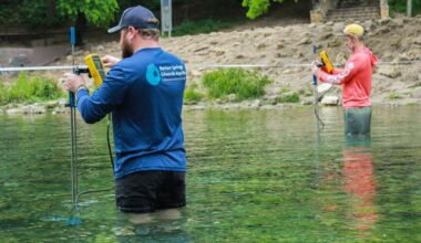 Two men stand in the translucent blue and green water of Barton Springs.
