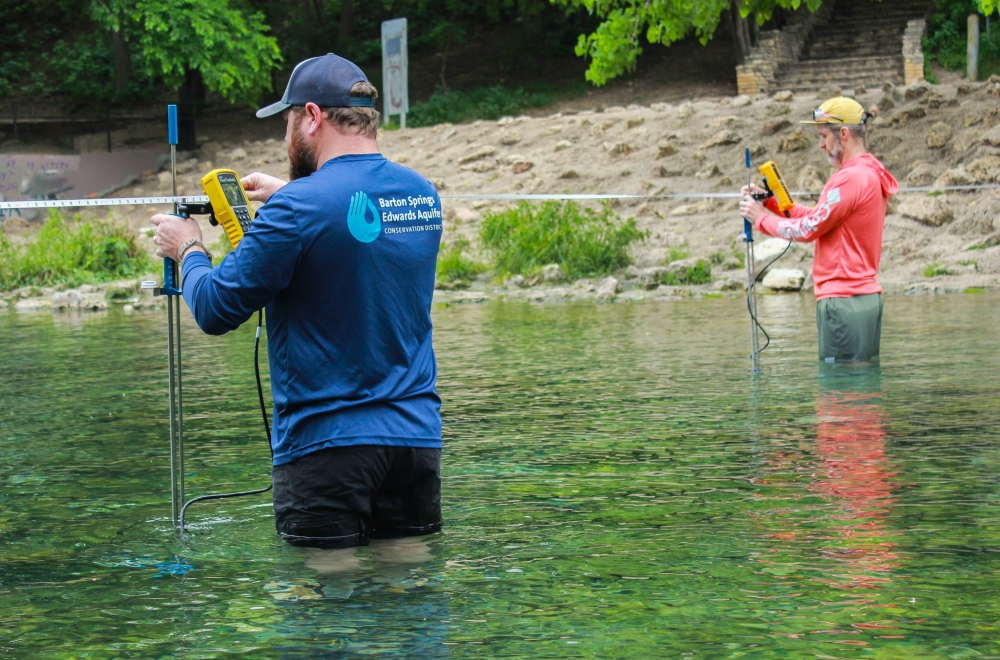 Two men stand in the translucent blue and green water of Barton Springs.