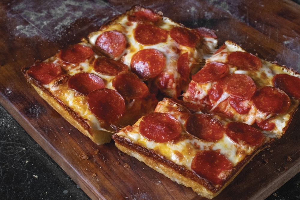 Overview of a pepperoni pizza on a dark brown cutting board.