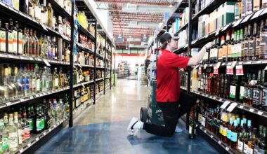 A Spec's employee wearing a red shirt neals to stock a wine shelf.