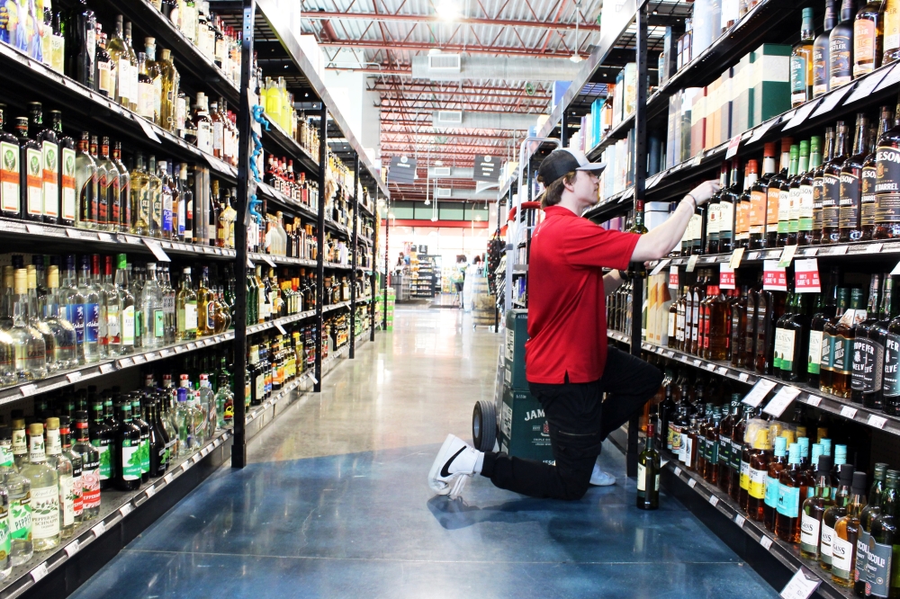 A Spec's employee wearing a red shirt neals to stock a wine shelf.