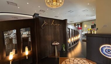 Interior of a restaurant featuring a Jashan decorative gold logo-sign on a dark brown wall. Other decor include ambient lamps and mosaic tile floor.