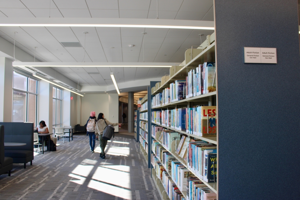 people walking near a shelf of books at a library