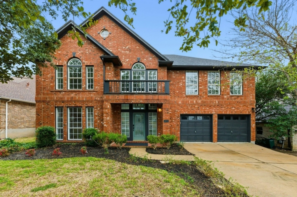Brick home with blue doorway and iron balcony in 78739