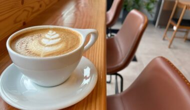 Coffee featuring leaf foam art in a white ceramic cup sitting in a white sauces on a brown wooden bar in a cafe.