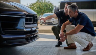 A Crash Champions team member and a patron kneel in front of a car while inspecting it.
