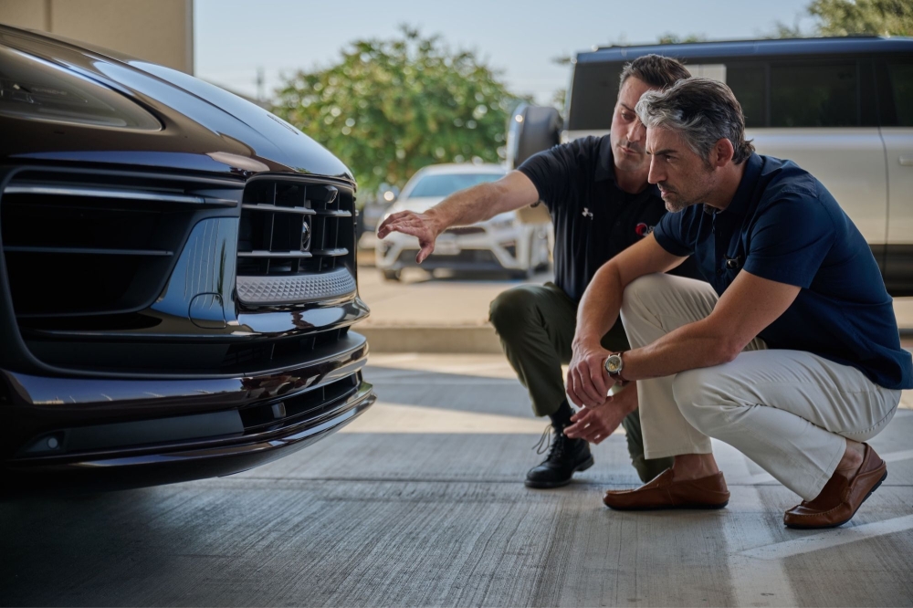 A Crash Champions team member and a patron kneel in front of a car while inspecting it.