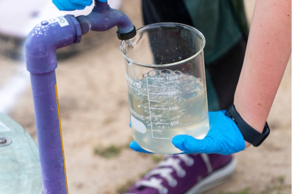 A worker fills a beaker with water from a land well.