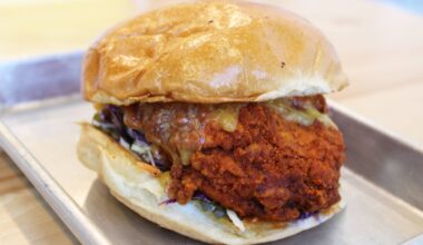 Side view of a fried chicken sandwich on a paper-lined metal tray.