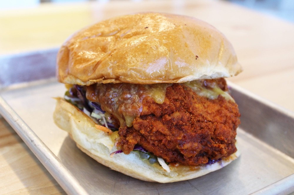 Side view of a fried chicken sandwich on a paper-lined metal tray.