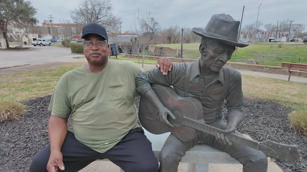 Jimmy Lipscomb sits next to a statue of his grandpa, Blues musician Mance Lipscomb in Mance...