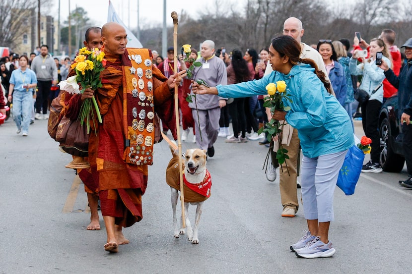 A woman hands a flower to Bhikkhu Pannakara as he walks with their dog Aloka as they head...