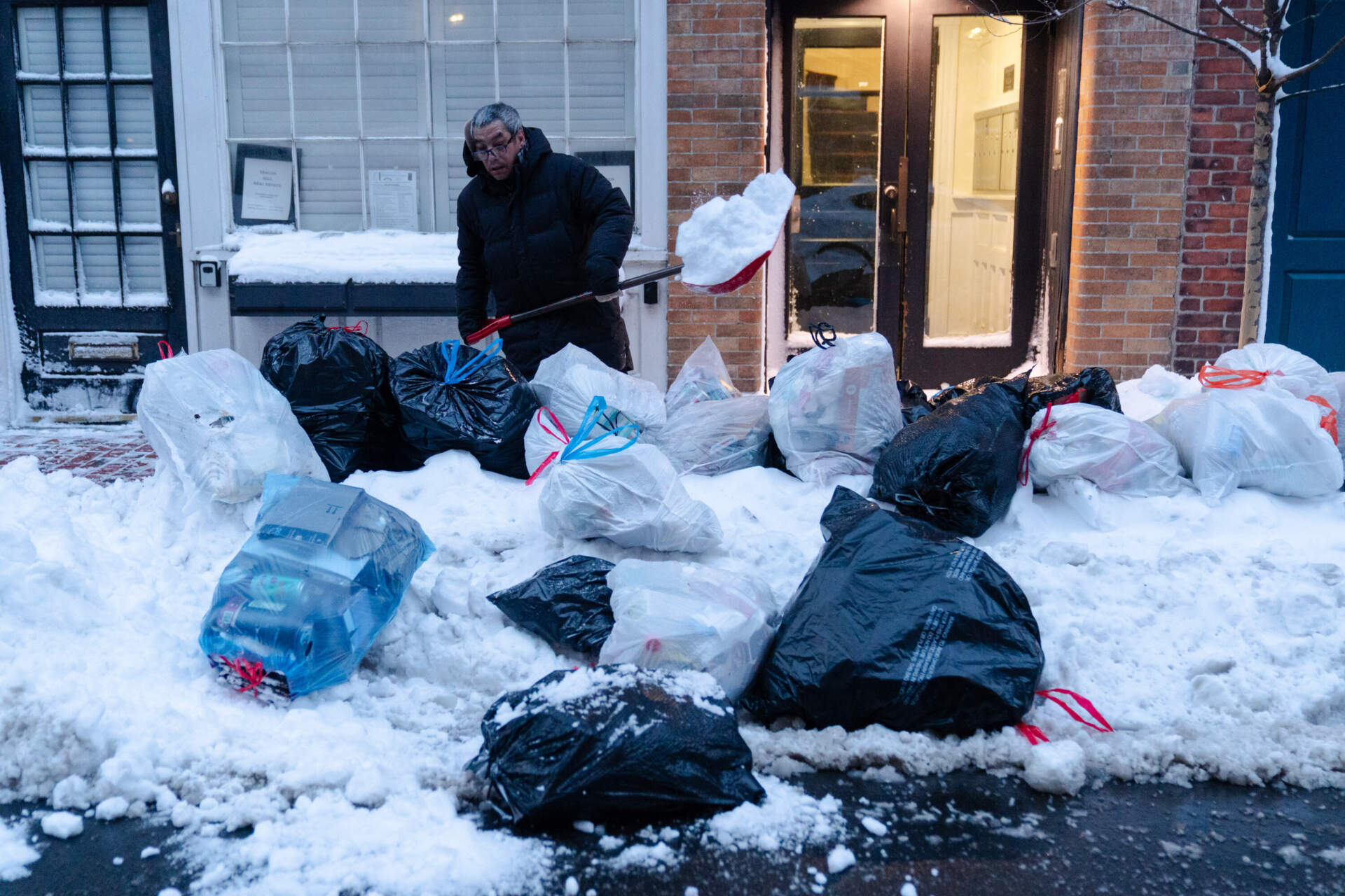 Key Lim, 55, removes snow from a sidewalk lined with trash bags in front of the laundromat that he manages on Tuesday, Feb. 24, 2026, in Boston. (Sophie Park/AP)