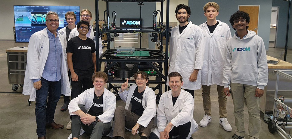 John Lauer (left) and members of the Adom Industries team gather around the company’s “workcell”—the core of its cloud-connected electronics prototyping factory. Lauer likens the system to “compute for atoms,” much like a server in a data center enables “compute for bits,” calling it the Amazon Web Services of electronics prototyping. The photo was taken shortly after a major presentation to a leading electronics company, following months of preparation.