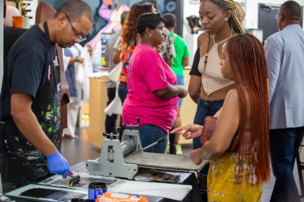 A printmaker demonstrates inking a plate for a small audience.