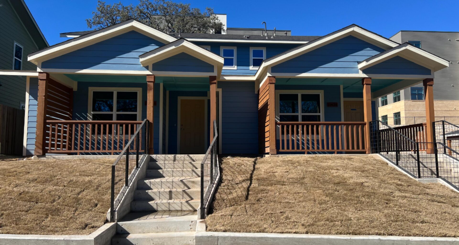Image a two-story duplex with two townhomes. The exterior is blue with brown wood railings and columns on the covered front porch.