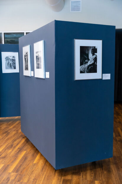 An installation image of framed black and white photographs by Earlie Hudnall, Jr. hanging on blue walls.