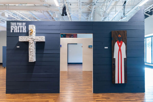 An installation image featuring a white cross sculpture and a painting of a choir boy.