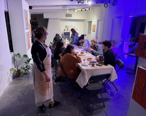 People congregating around a long table working on ceramics.