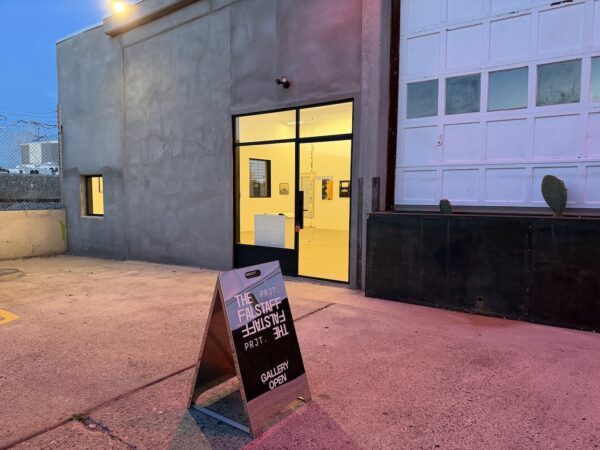 A snadwich board reading "The Falstaff Project" in front of a lit gallery space.