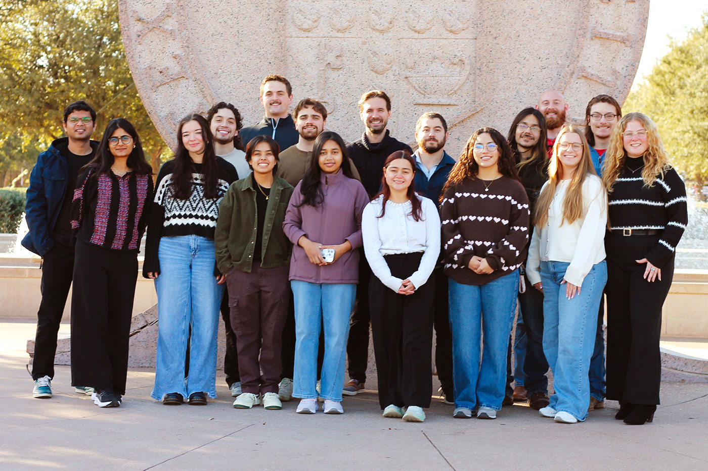 Wendy Galvan, front left in a green button-up shirt and back top, stands with the rest of the research group in Joshua Tropp’s lab.