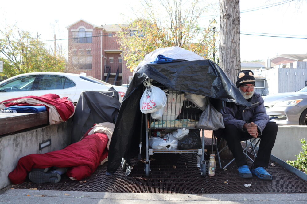 Dave sits on a chair next to a shopping cart full of his belongings on Bagby Street in Houston's Midtown. March, 2025.