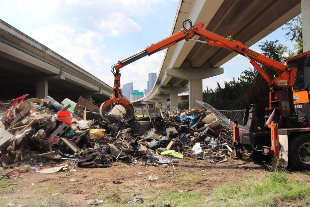 A crane removes belongings and debris from a homeless encampment off Nance Street under US-59 in Houston.