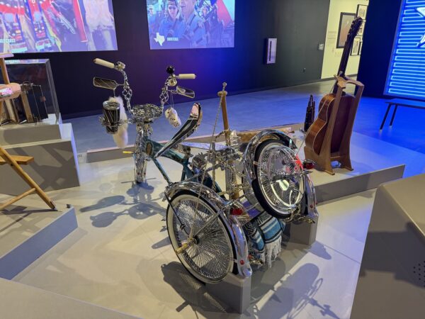 A lowrider tricycle elaborately decorated with chrome, a baseball bat, and a folded blanket.