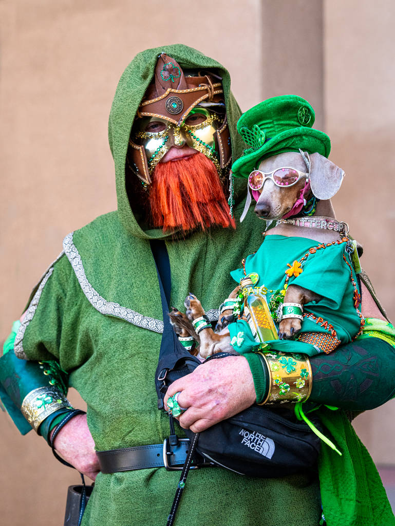 Image shows a man in Irish clothing and a fake orange beard holding a dog also in Irish clothing.