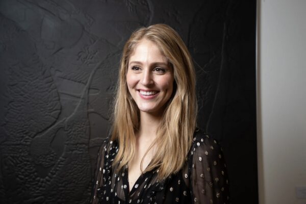 A portrait of art fair director Kelly Cornell, smiling in front of a black painting.
