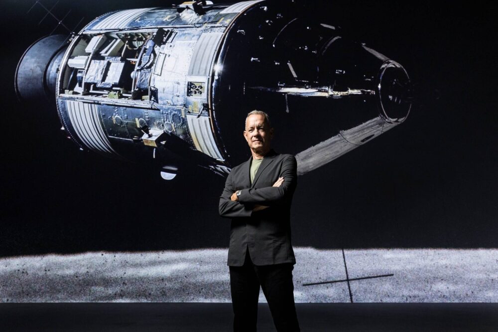 Photo of actor Tom Hanks in front of an image of a spacecraft.