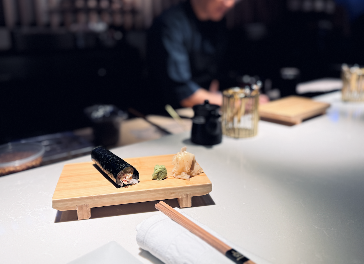 A handroll sitting on a plate on an elegant black bar.