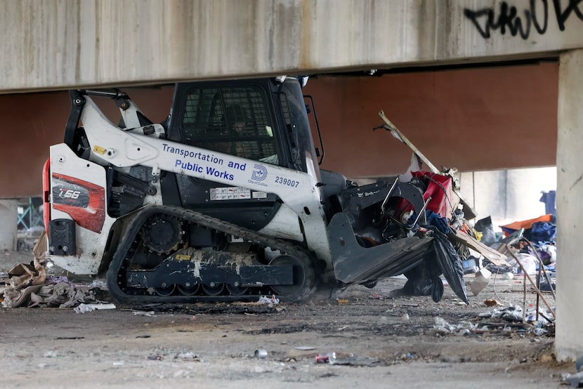 A City of Dallas skid-steer clears a homeless encampment from underneath a bridge, Thursday,...