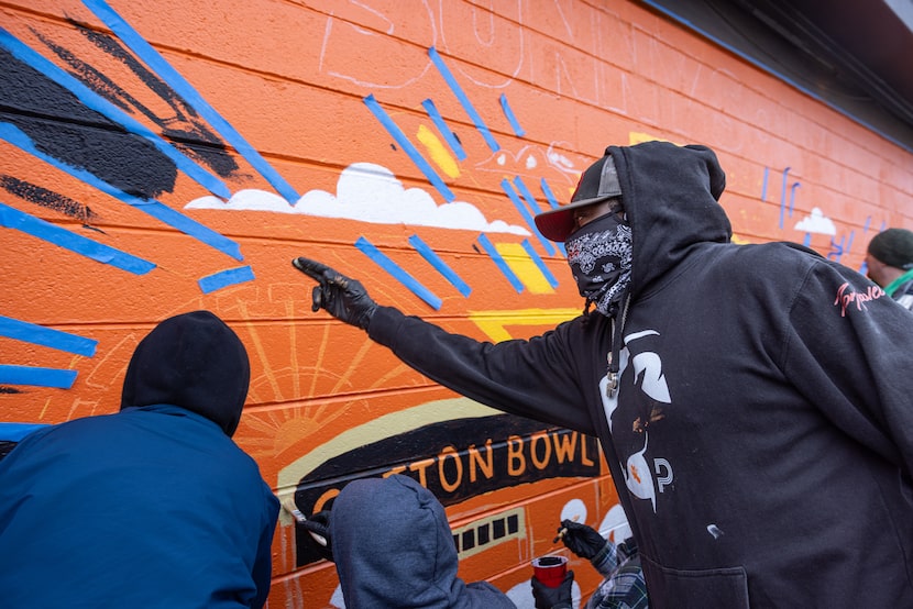 Artist Theo Ponchaveli directs volunteers helping paint a mural he created as an homage to...