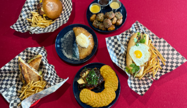 Rising Tides dishes, including a dessert empanada and smash burger, laid out over a pool table.