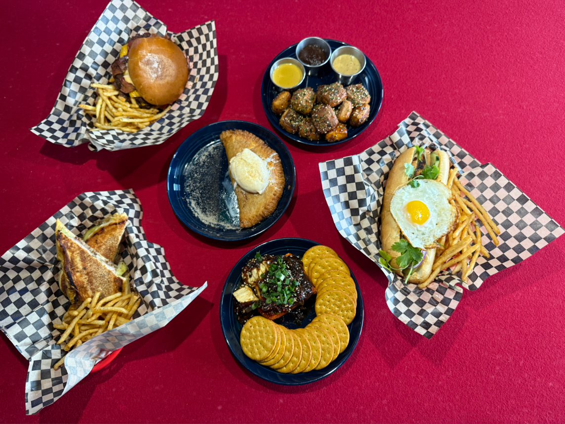 Rising Tides dishes, including a dessert empanada and smash burger, laid out over a pool table.