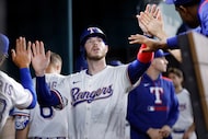 Texas Rangers Jonah Heim is congratulated by teammates in the dugout after scoring on Adolis...
