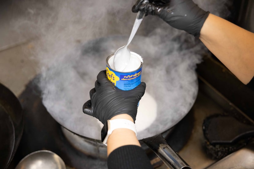 Irean Wongchingchai adds coconut milk as she cooks red curry with chicken on a wok at her...