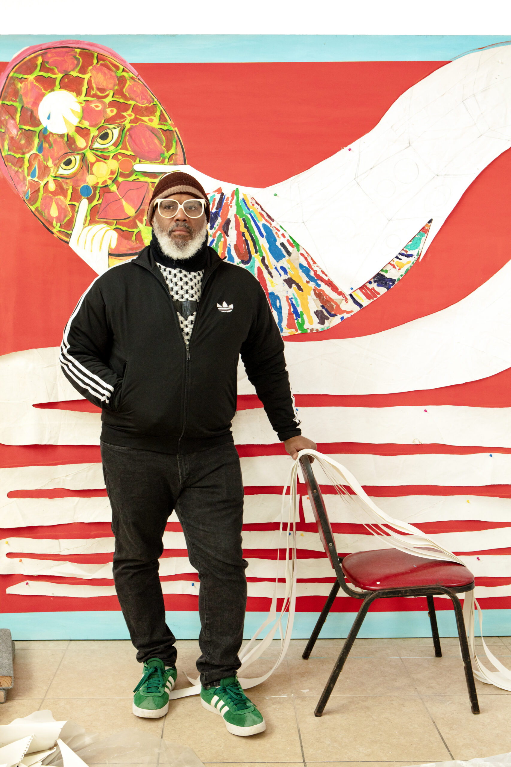 A photograph of artist Trenton Doyle Hancock in his studio in front of a large painting in progress.