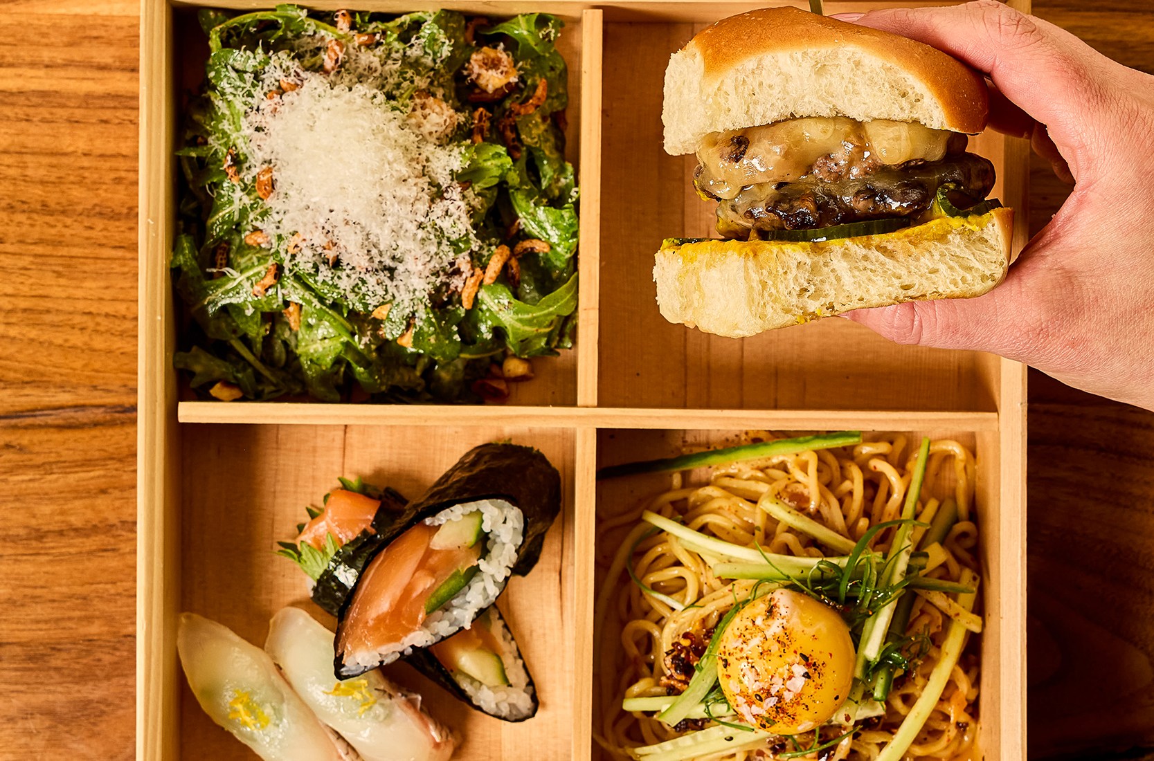 A lunch box has a sandwich, salad, sushi, and shredded vegetables.