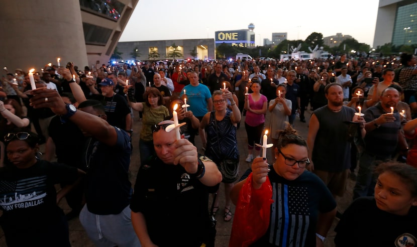 Dallas police officers and other people hold candles during a vigil hosted by the Dallas...