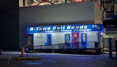 A bail bonds office with a blue-and-white sign is lit up at night. A ramp leads up to the door.