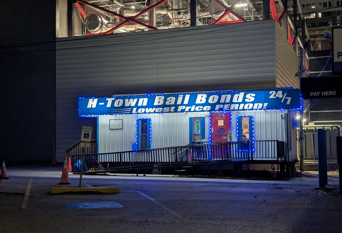 A bail bonds office with a blue-and-white sign is lit up at night. A ramp leads up to the door.