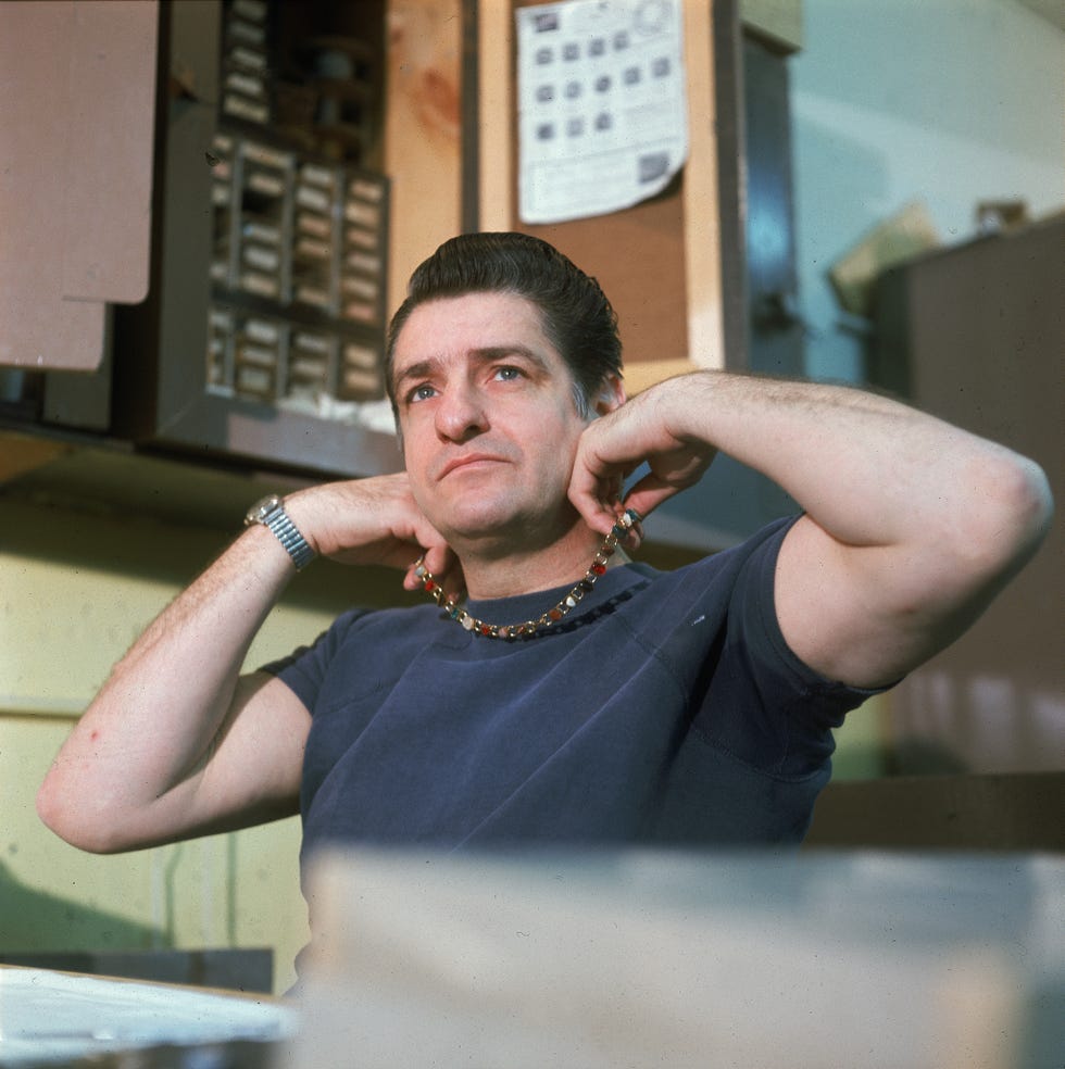 a man holds a necklace around his neck as he sits on a chair inside an office room