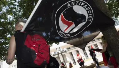 A person holds a black flag that says "ANTIFASCIST ACTION"