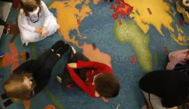 An overhead view shows young children interacting as they sit on a rug that looks like a world map.