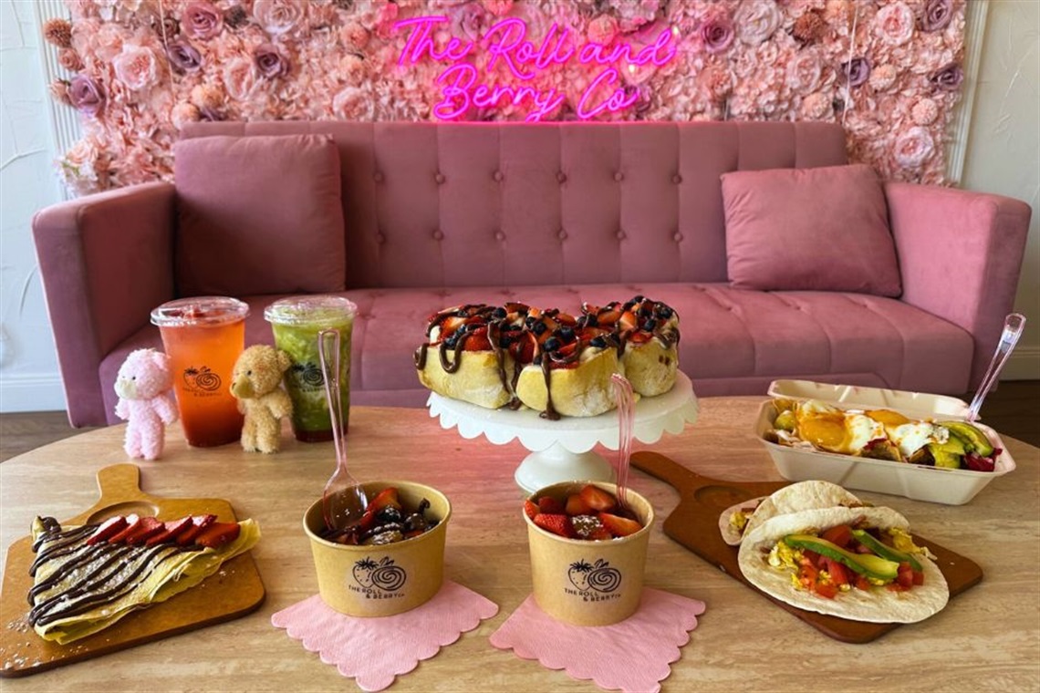 a table with different sweets and drinks in a background with a pink couch and a flower wall