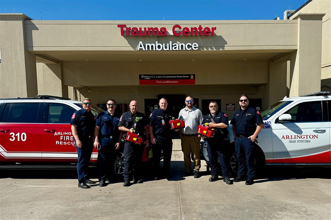 Firefighters stand in front of a trauma center holding medical boxes.